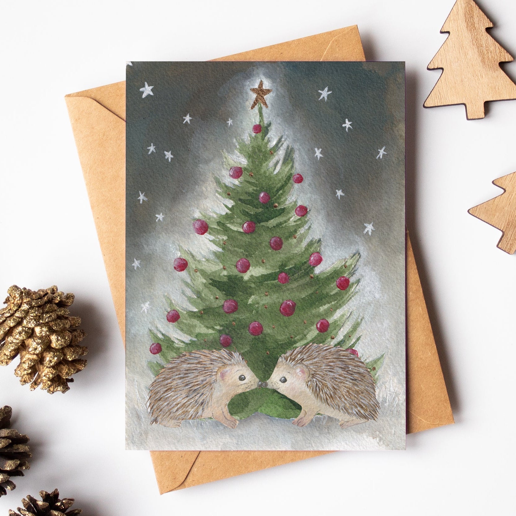 Christmas card with hedgehogs and a tree, surrounded by pinecones and wooden trees on a white background