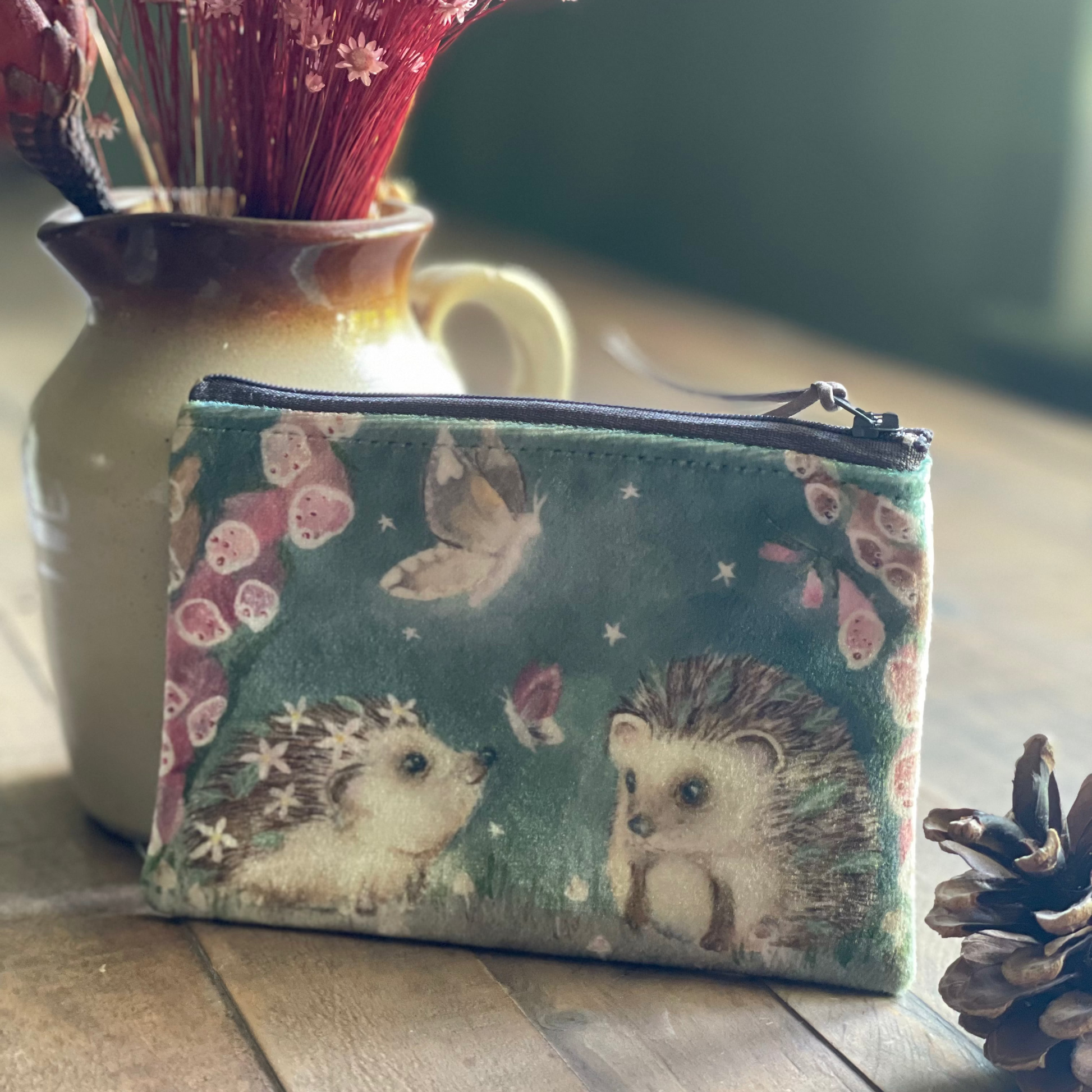 Small pouch with hedgehog design on a wooden surface with a vase of flowers in the background