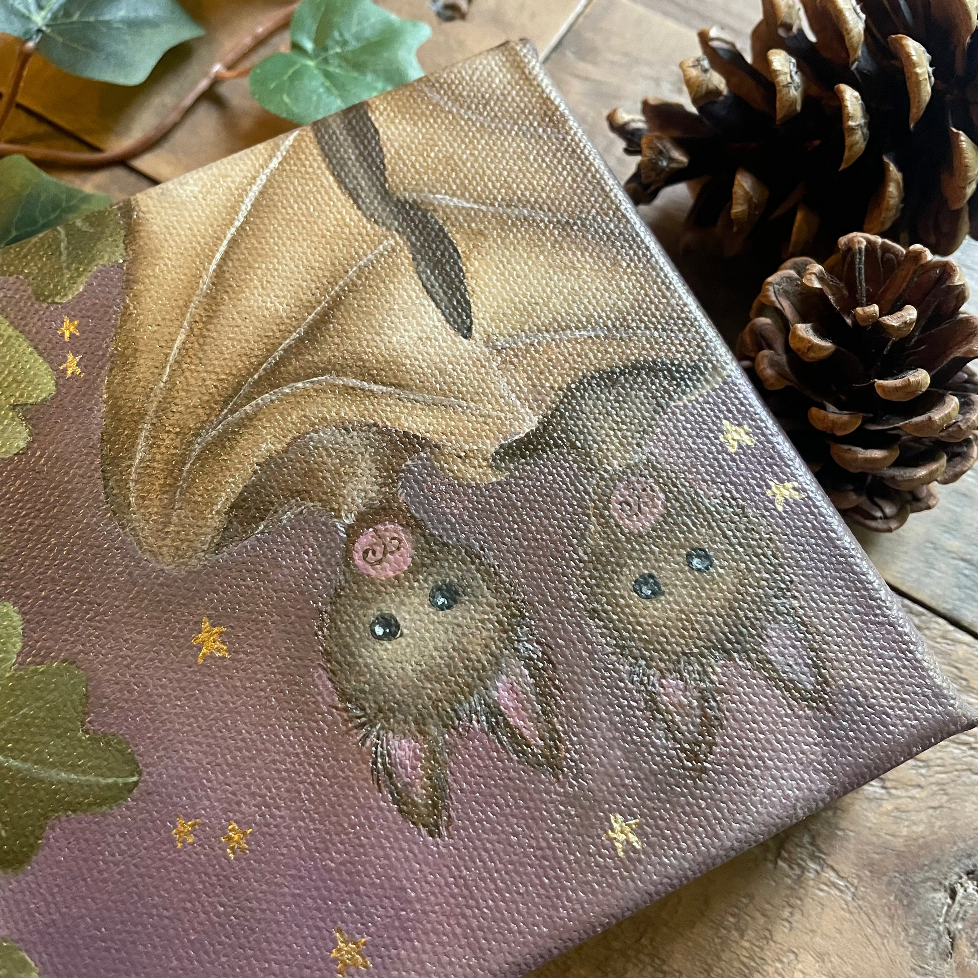 Canvas print with a bat design on a wooden surface with pinecones and leaves.