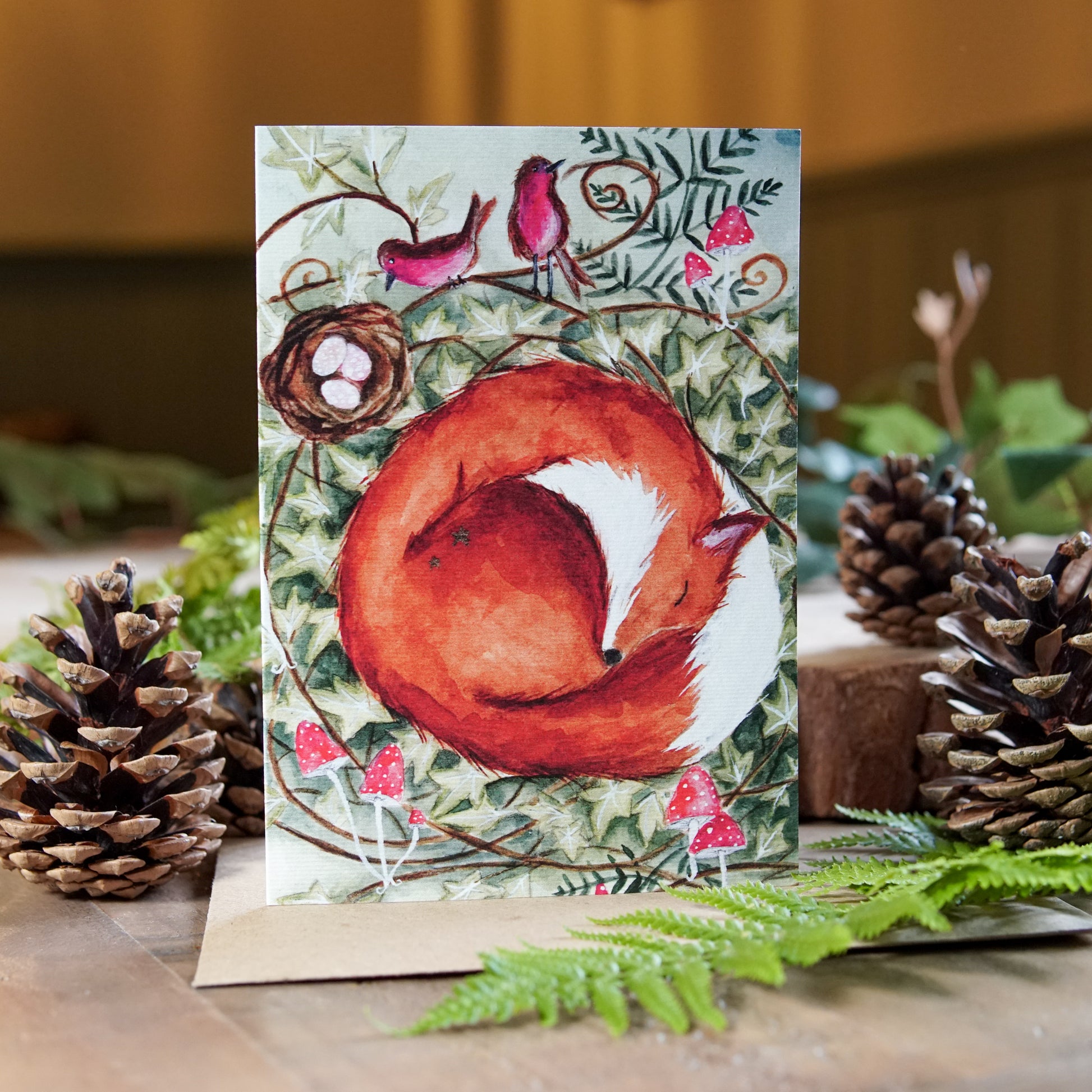 Sleepy fox curled up in a woodland nest among toadstools on a greeting card