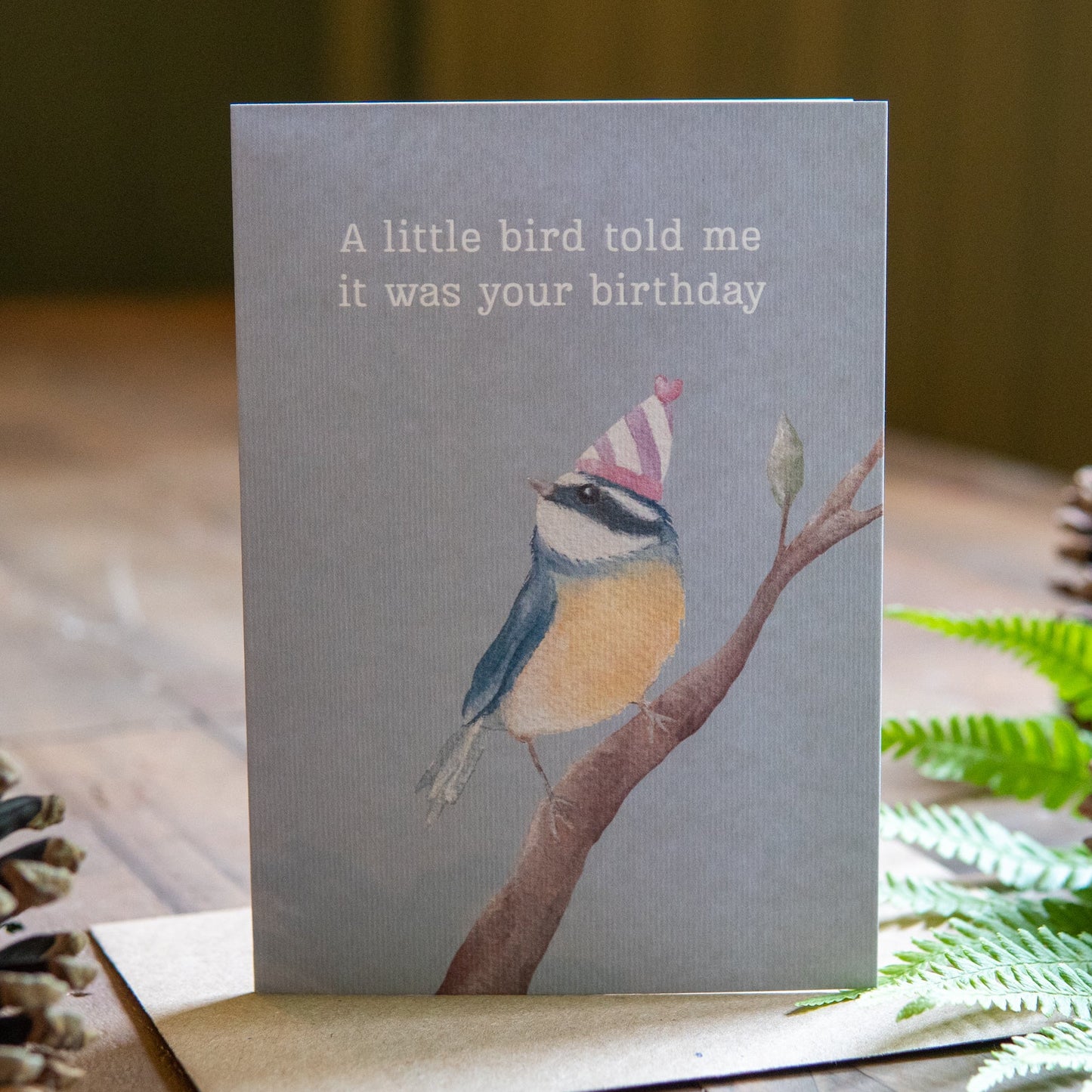 Greeting card with a bird illustration and text on a wooden surface with decorative elements.