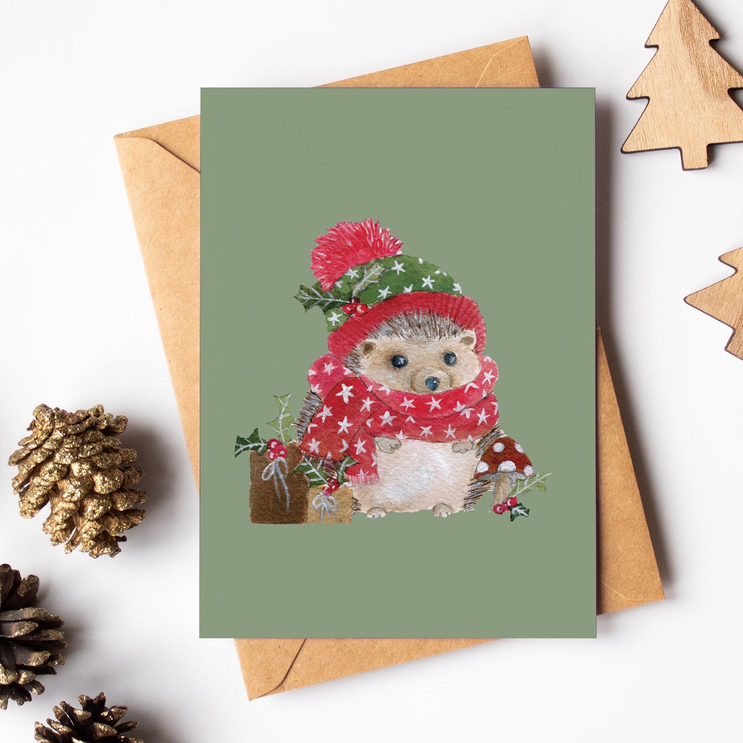 Christmas-themed greeting card with a hedgehog illustration, surrounded by pinecones and wooden trees on a white background.
